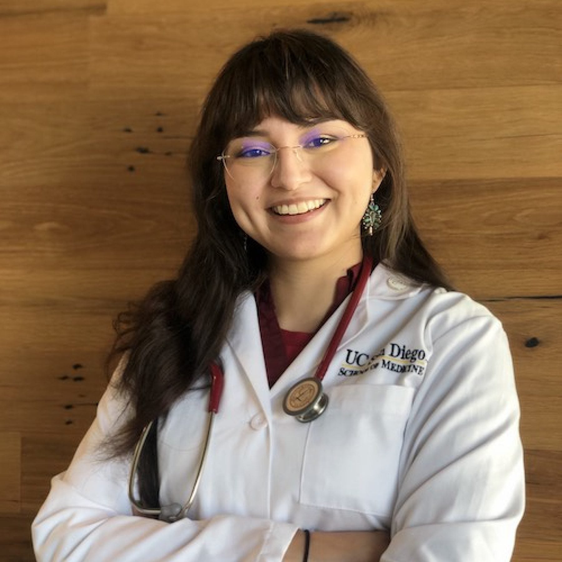 Yasmin Zuch smiles while folding her arms wearing a doctor's white coat and glasses