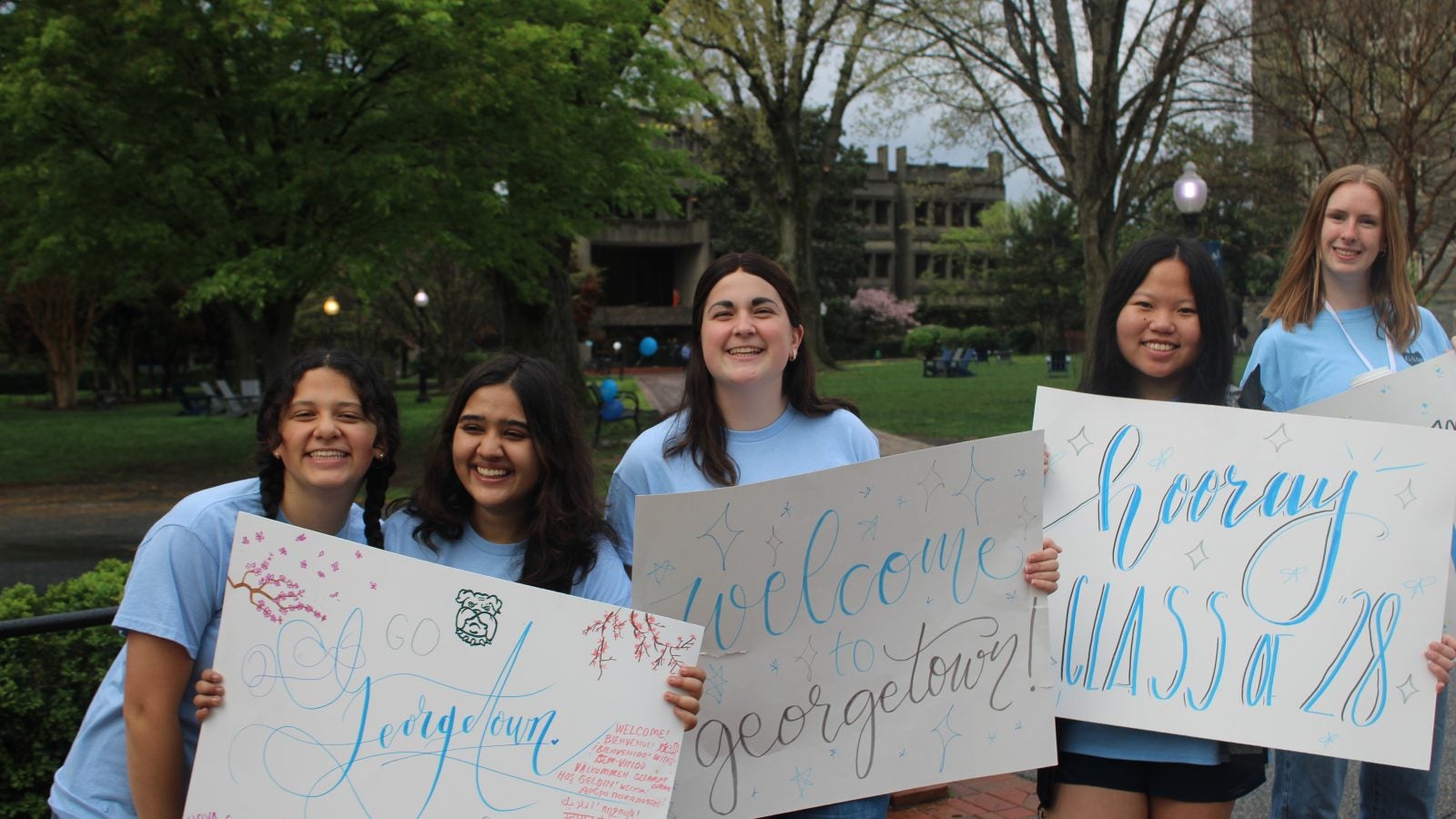 Young women in blue shirts holding welcome signs